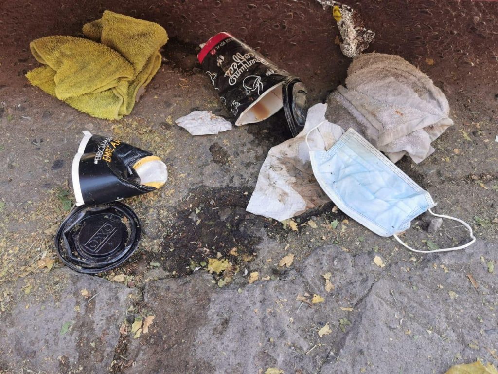 Un cubrebocas junto a vasos de café tirados en la calle